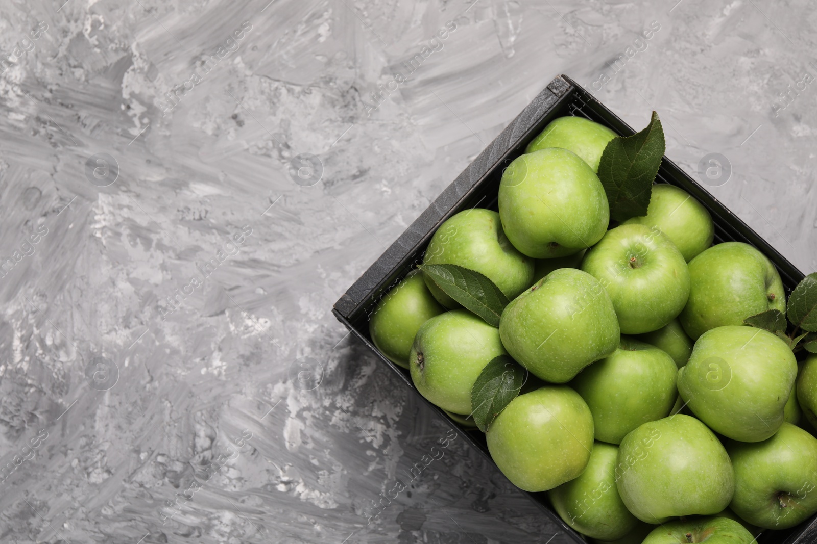 Photo of Fresh green apples in crate on grey textured table, top view. Space for text