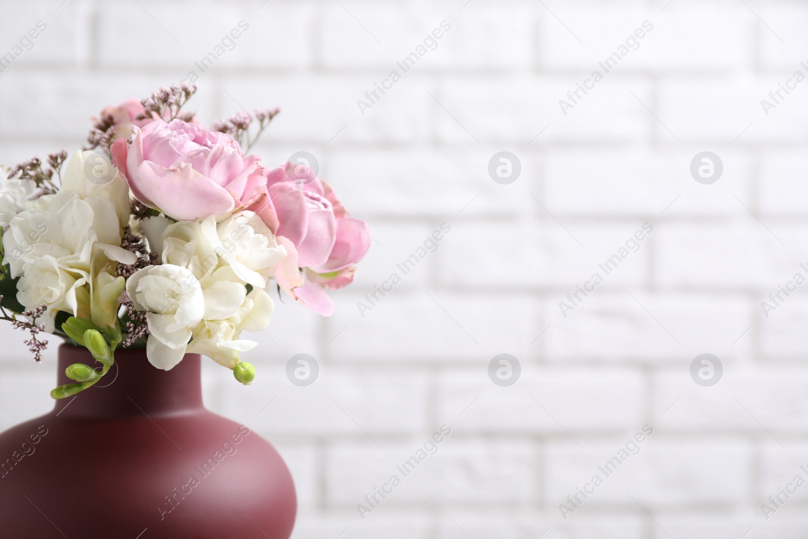 Photo of Beautiful bouquet with roses against white brick wall, closeup. Space for text