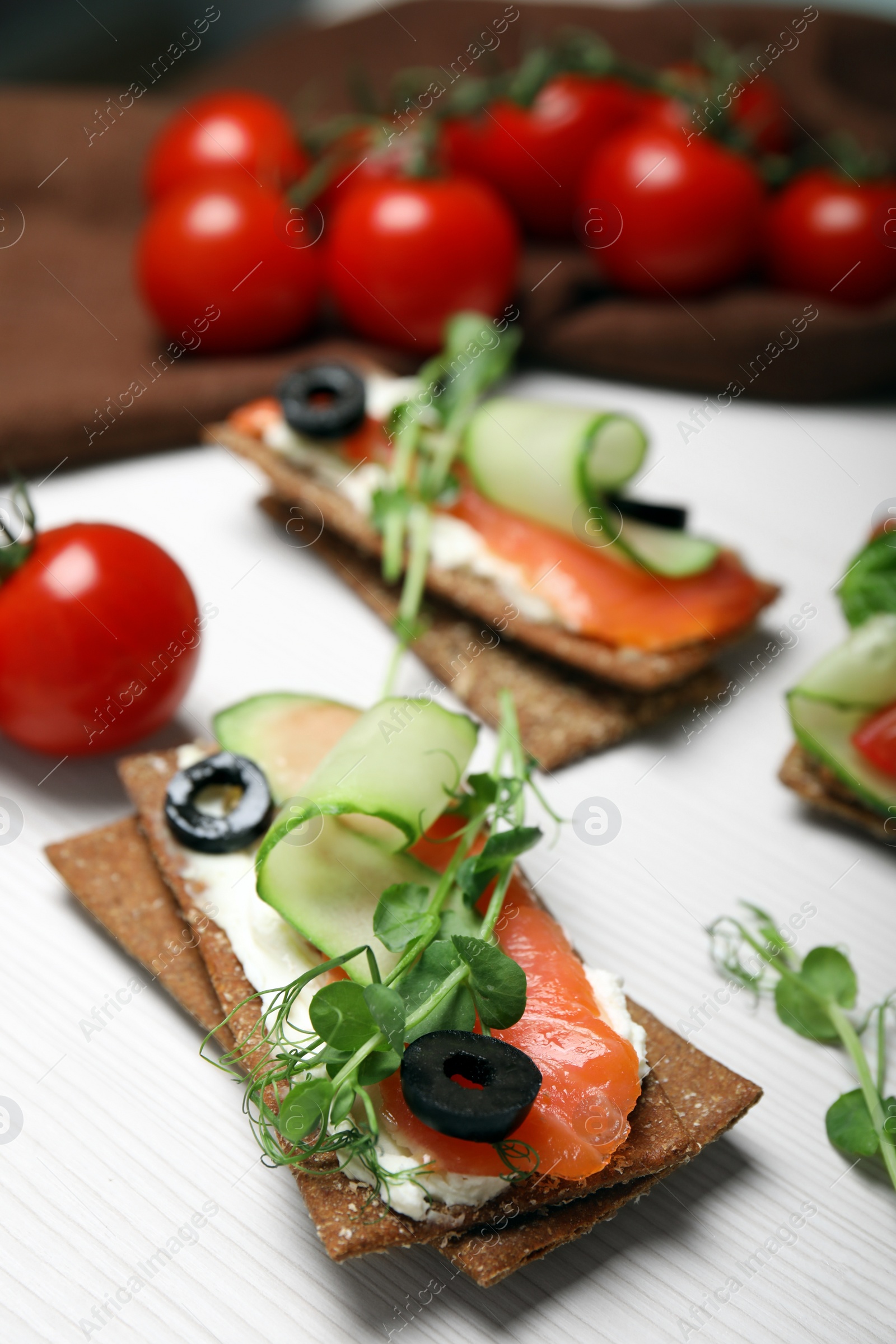 Photo of Tasty rye crispbreads with salmon, cream cheese and vegetables on white wooden table, closeup