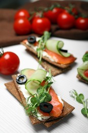 Photo of Tasty rye crispbreads with salmon, cream cheese and vegetables on white wooden table, closeup