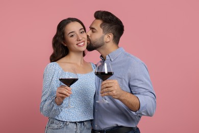 Photo of Man kissing his smiling girlfriend on pink background