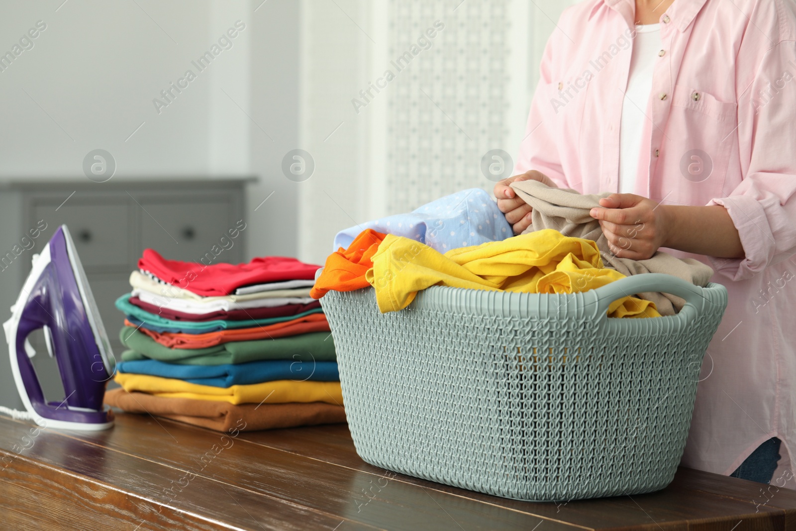 Photo of Woman with basket full of clean laundry at wooden table indoors, closeup