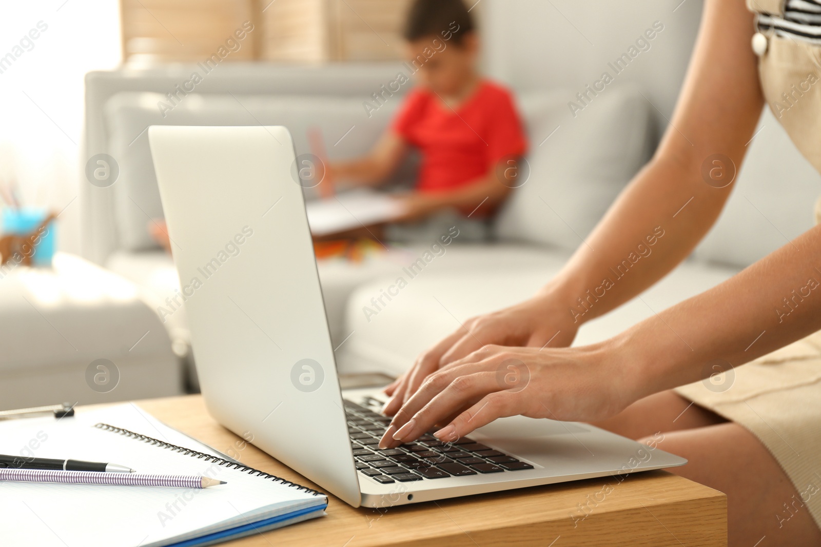 Photo of Young woman working on laptop while son drawing in living room, closeup. Home office concept