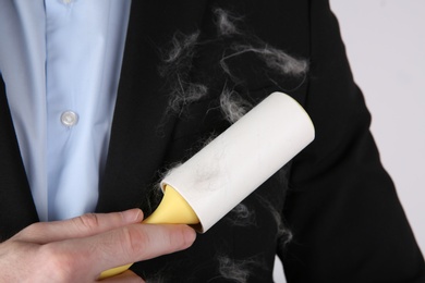 Photo of Man removing hair from black jacket with lint roller on  light grey background, closeup