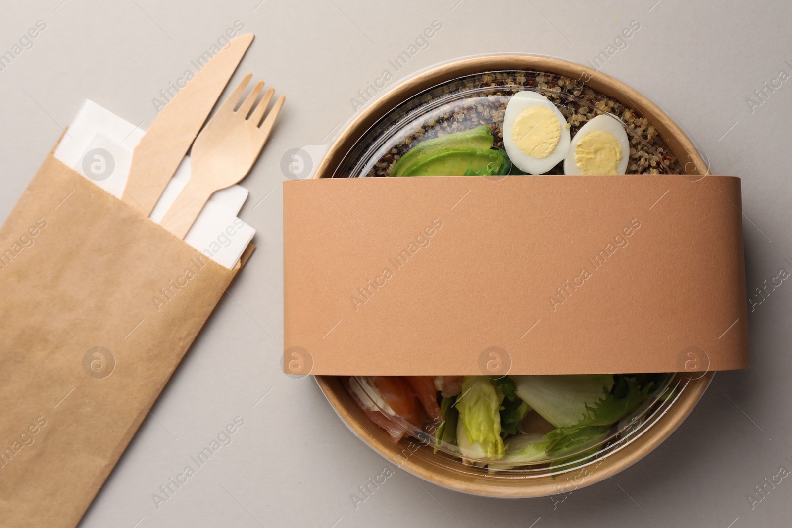 Photo of Tasty food in container with wooden fork and knife on light background, flat lay. Space for text