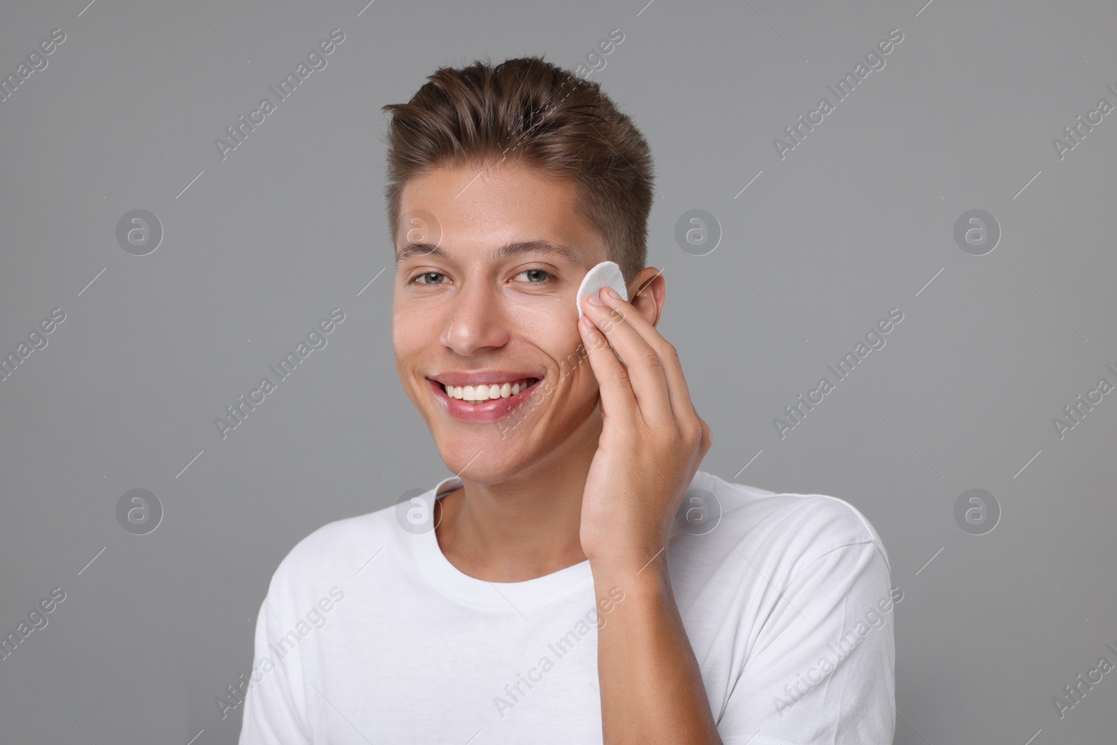 Photo of Handsome man cleaning face with cotton pad on grey background