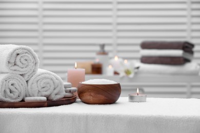 Photo of Spa composition with rolled towels and burning candles on massage table in wellness center, space for text
