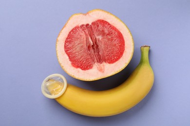 Photo of Banana with condom and half of grapefruit on violet background, flat lay. Safe sex concept