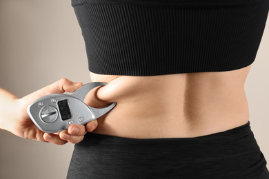 Photo of Nutritionist measuring woman's body fat layer with digital caliper on beige background, closeup