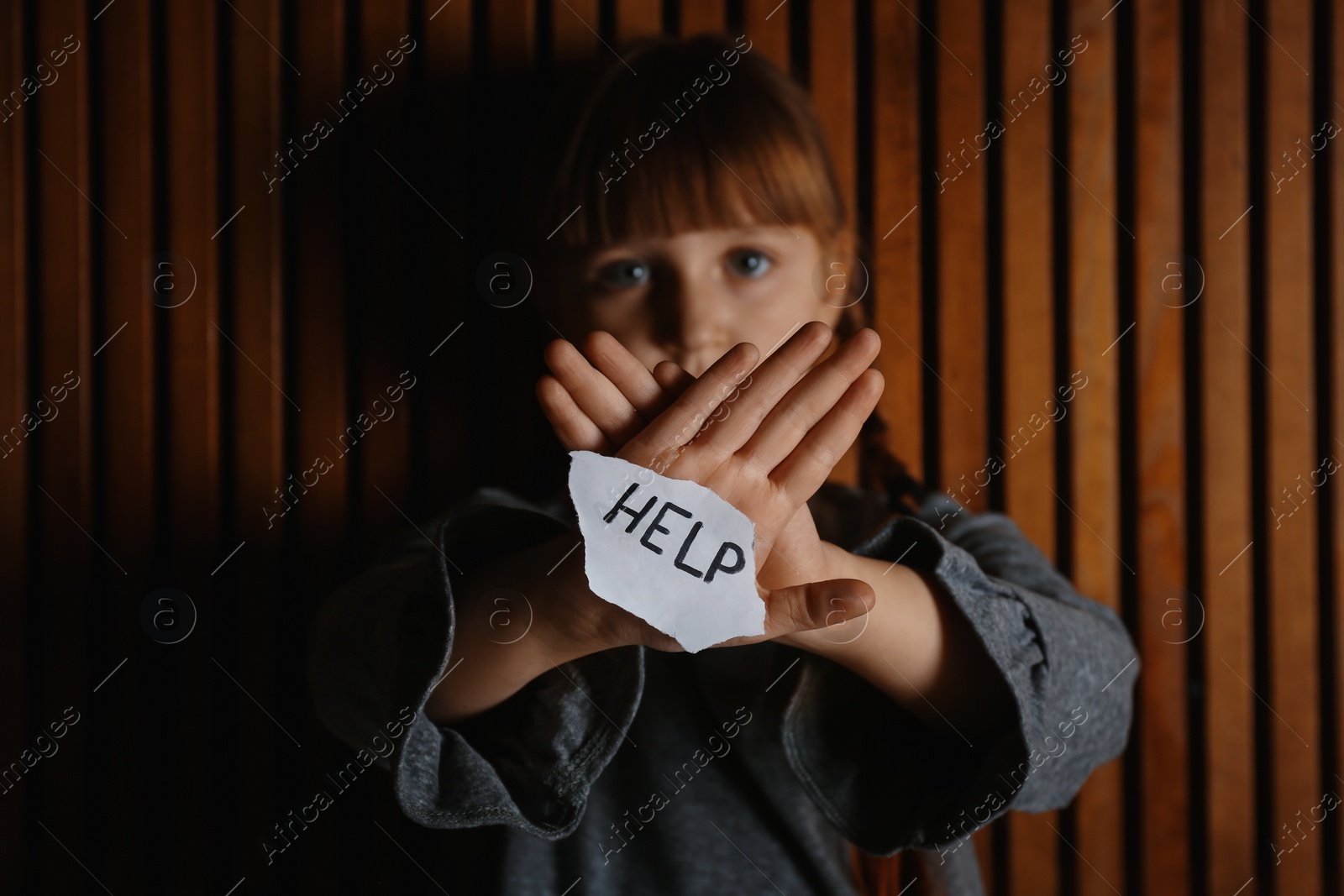 Photo of Sad little girl with sign HELP on wooden background. Child in danger