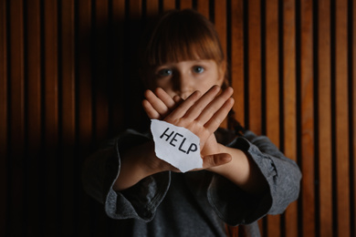 Sad little girl with sign HELP on wooden background. Child in danger