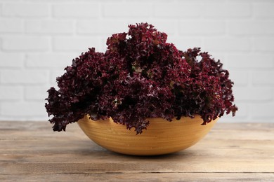 Photo of Bowl with fresh red coral lettuce on wooden table