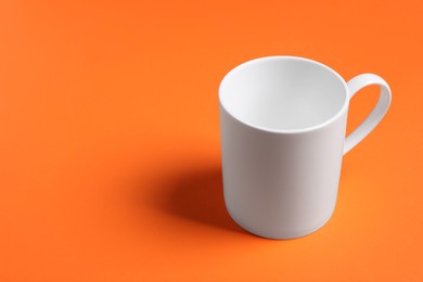 Photo of One white ceramic mug on orange background, space for text