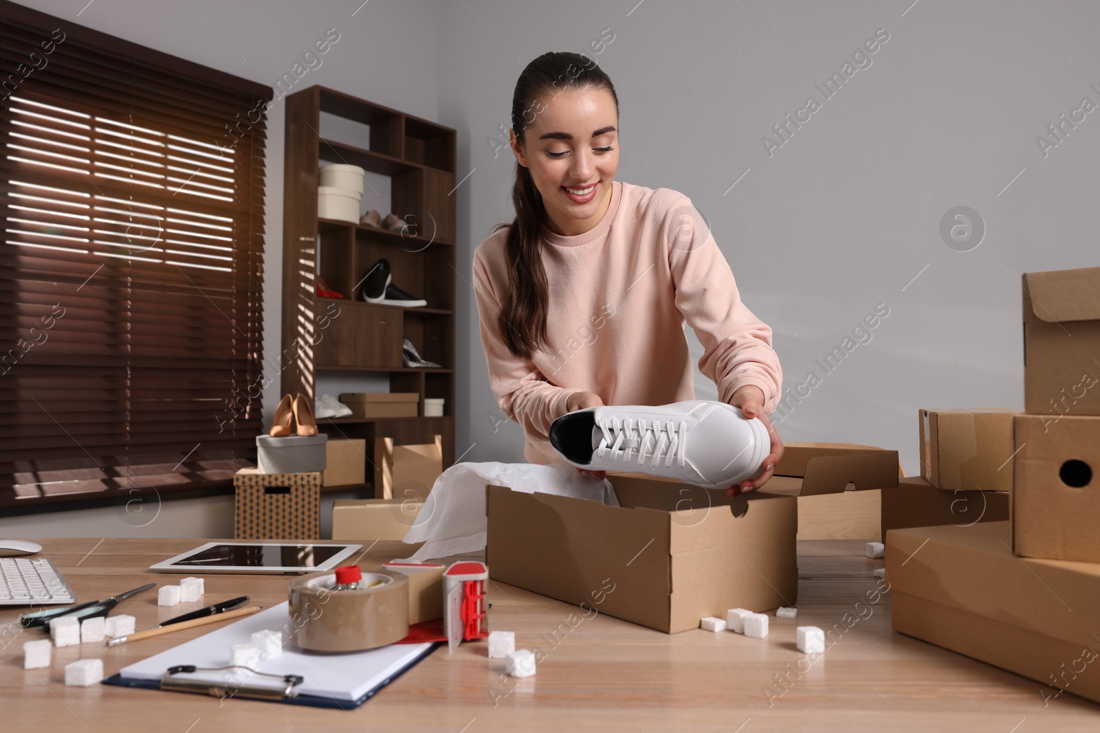 Photo of Seller packing shoes into cardboard box at table in office. Online store