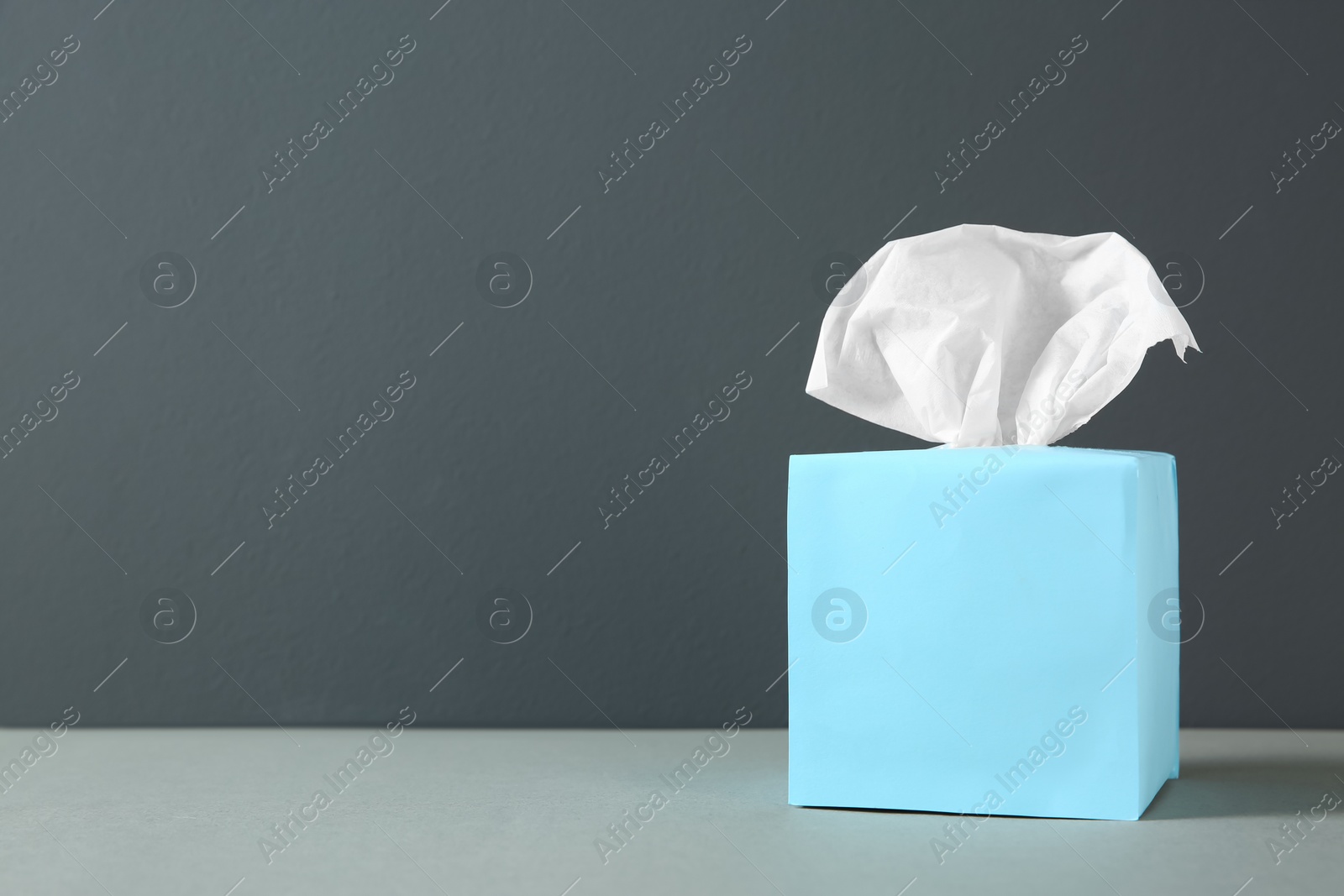 Photo of Box with paper tissues on light grey table. Space for text