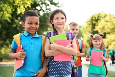 Photo of Cute little children with backpacks and notebooks outdoors. Elementary school