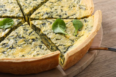 Cut delicious spinach pie with server on wooden table, closeup