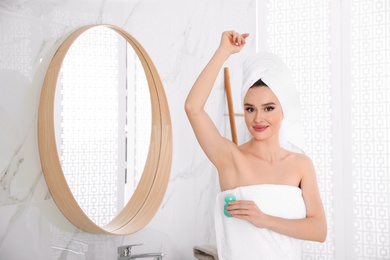 Photo of Beautiful young woman applying deodorant after shower in bathroom