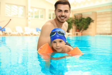 Happy father teaching his son to swim with inflatable sleeves in indoor pool