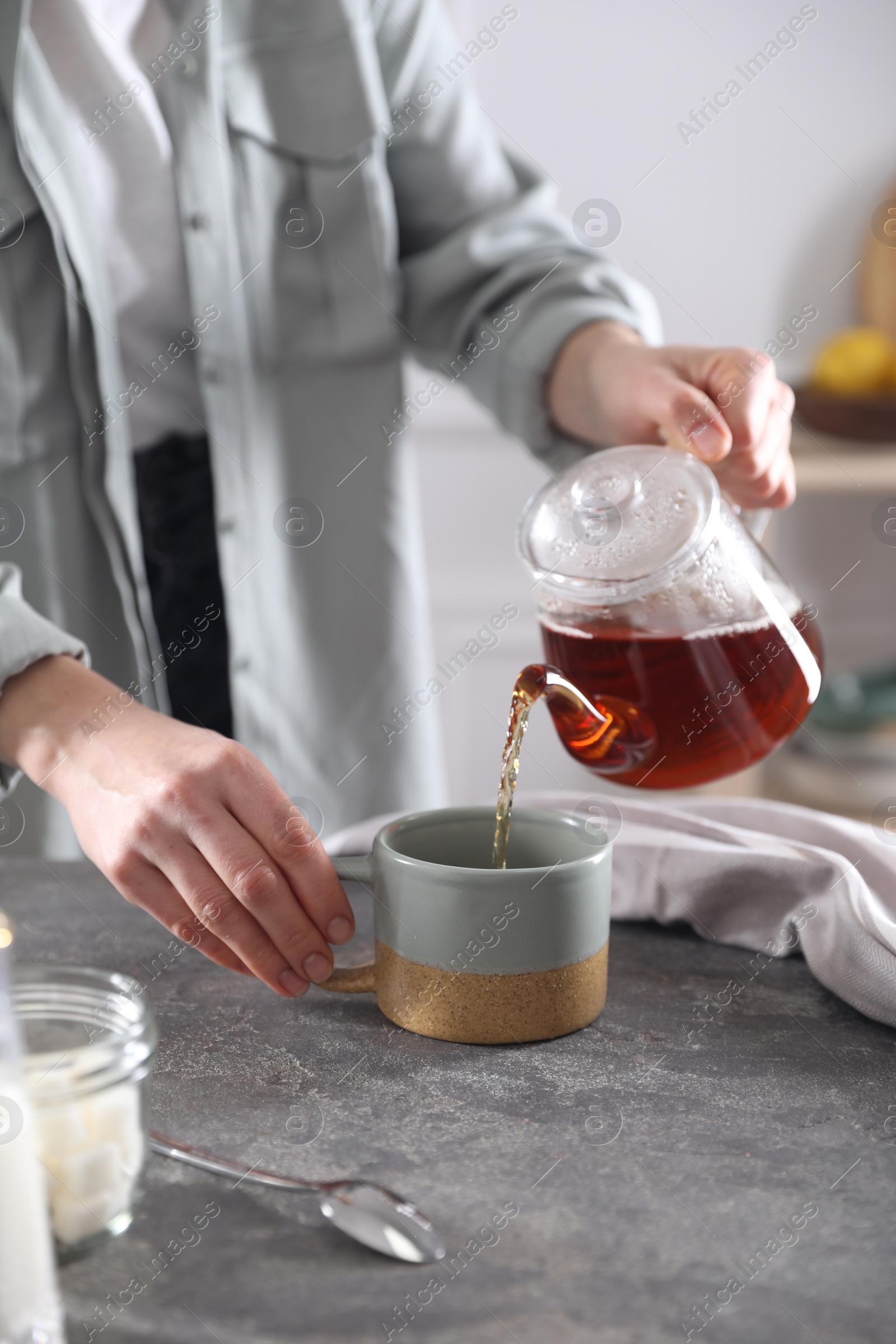 Photo of Woman pouring hot tea into cup at grey table, closeup