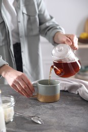 Photo of Woman pouring hot tea into cup at grey table, closeup