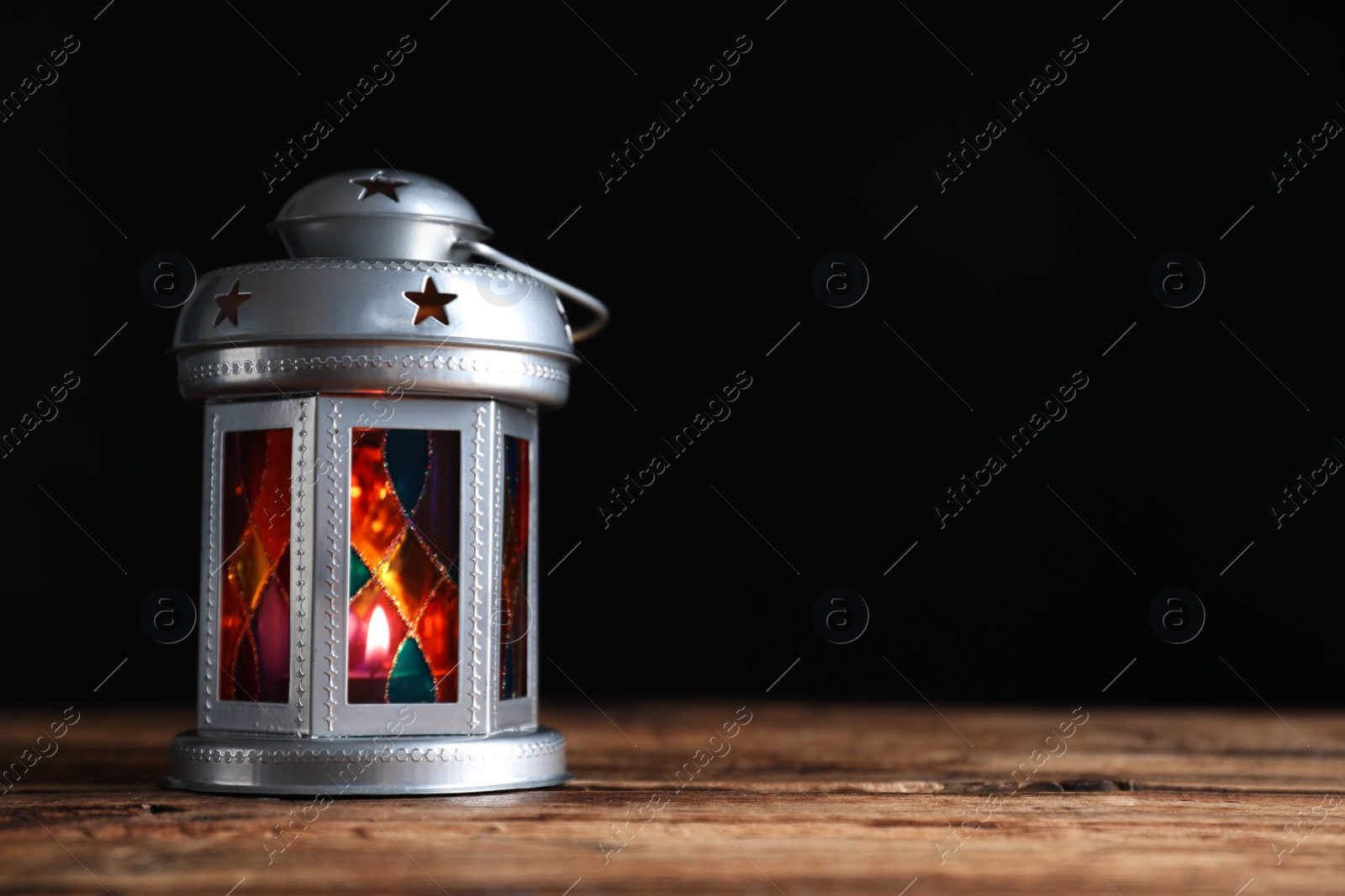 Photo of Decorative Arabic lantern on wooden table against black background, space for text