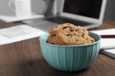 Photo of Bowl with chocolate chip cookies on wooden table in office, closeup