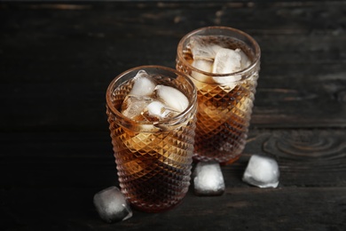 Glasses of refreshing cola with ice cubes on wooden background