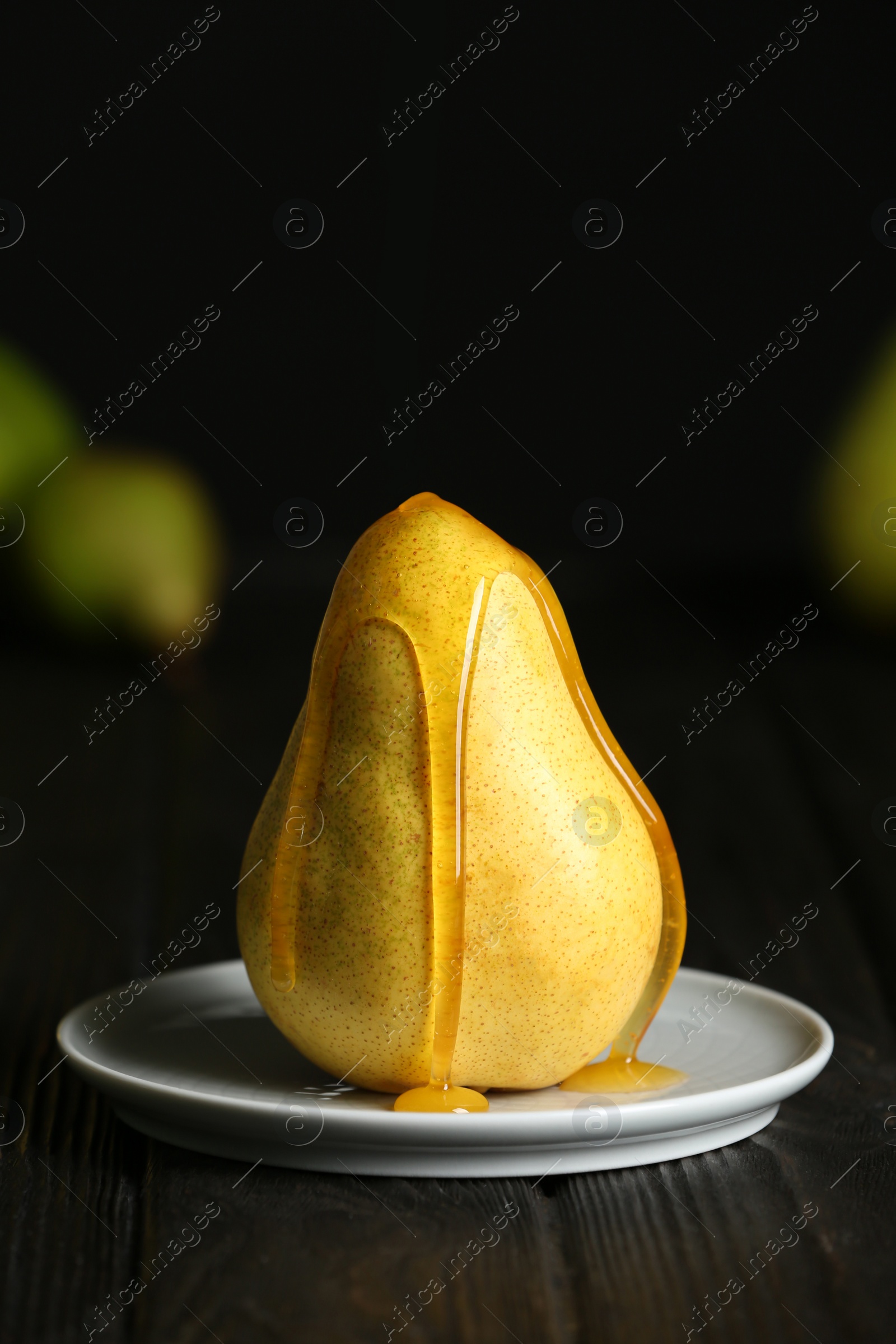 Photo of Pouring sweet syrup onto fresh ripe pear on table against blurred background