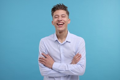 Photo of Young man with crossed arms laughing on light blue background