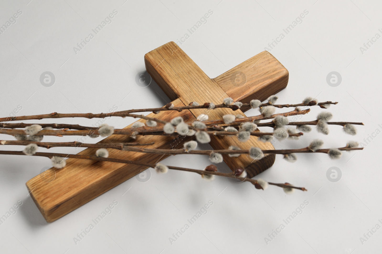 Photo of Wooden cross and willow branches on light grey background. Easter attributes