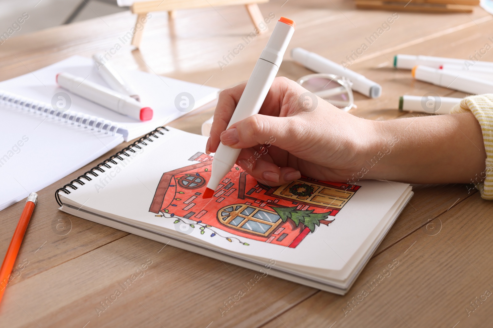 Photo of Woman drawing in sketchbook with felt tip pen at wooden table, closeup