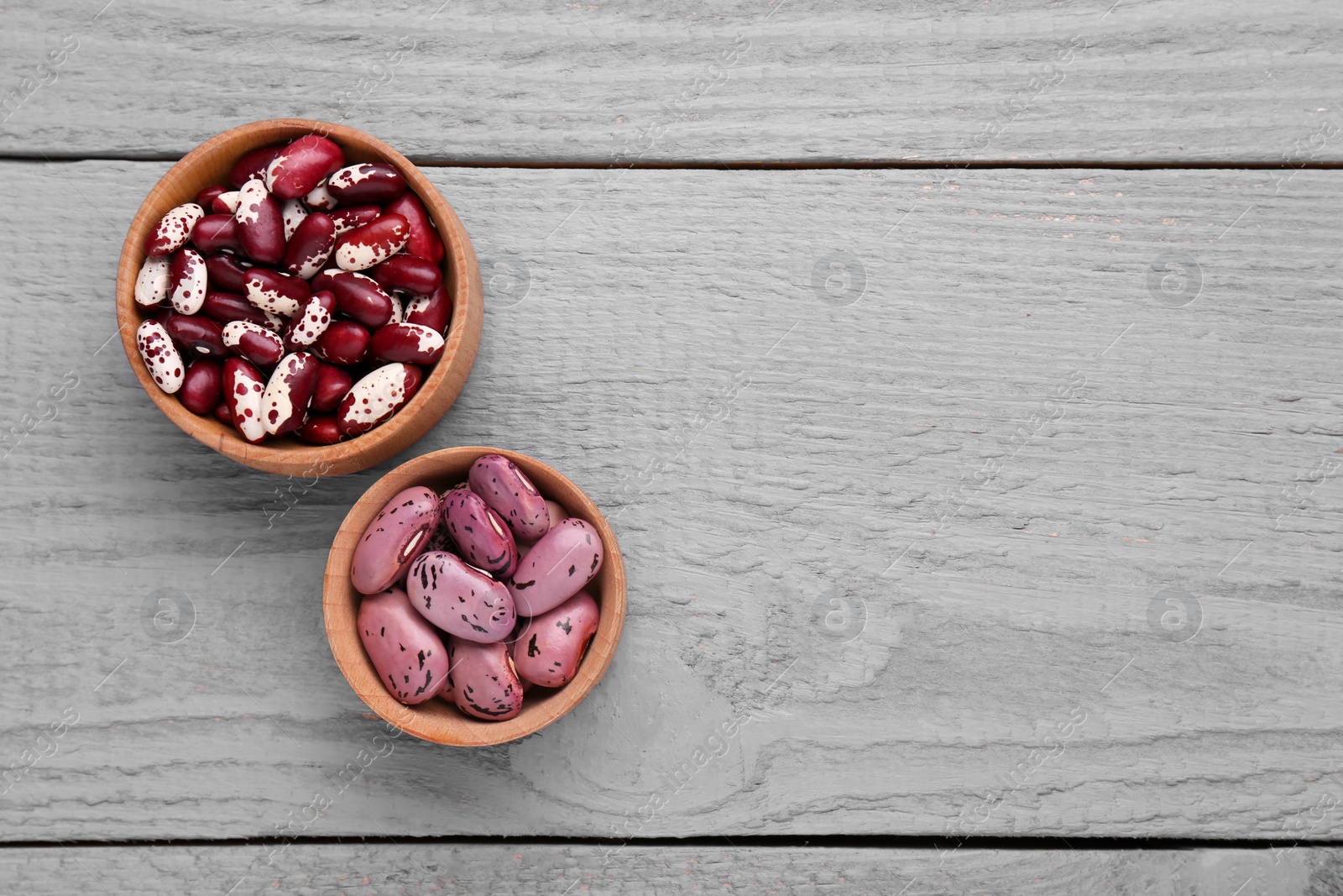 Photo of Different kinds of dry kidney beans on grey wooden table, flat lay. Space for text