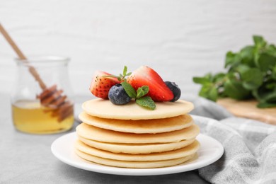 Photo of Stack of tasty pancakes with fresh berries and mint on light grey table, closeup