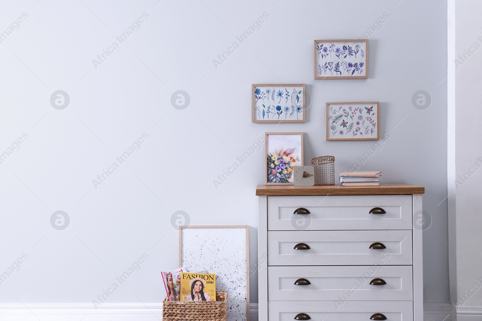 Photo of Wooden chest of drawers with books and decor near white wall in room, space for text. Interior design