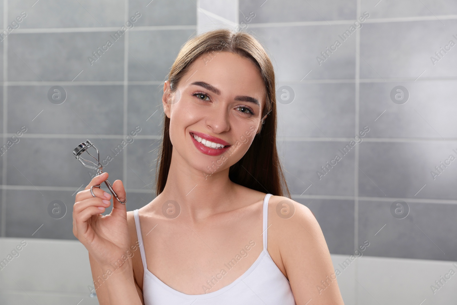 Photo of Happy young woman with eyelash curler indoors