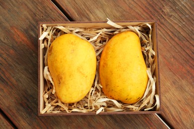 Delicious ripe yellow mangoes in box on wooden table, top view