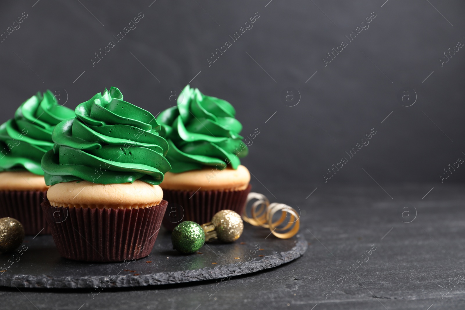 Photo of Delicious cupcakes with green cream and Christmas decor on black table. Space for text