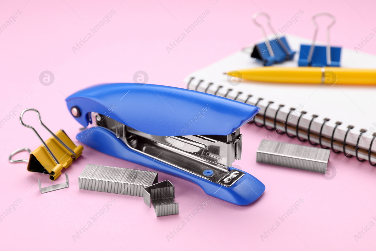 Photo of New bright stapler with stationery on pink background