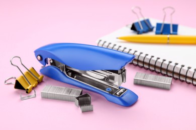 New bright stapler with stationery on pink background