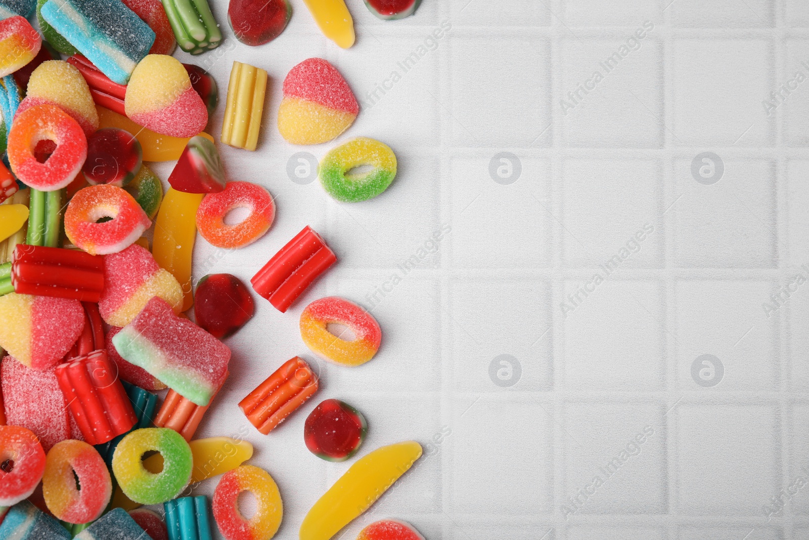 Photo of Many tasty colorful jelly candies on white tiled table, flat lay. Space for text