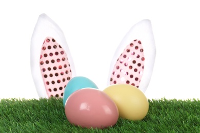 Cute decorative Easter bunny ears and dyed eggs on green grass against white background