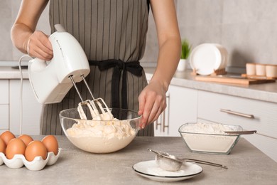 Photo of Woman whipping white cream with mixer at light grey table in kitchen, closeup