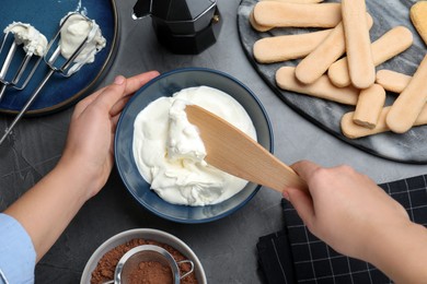 Photo of Woman making tiramisu cake at black table, top view