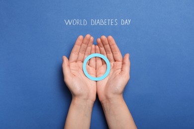 Woman holding blue paper circle near text World Diabetes Day on color background, top view