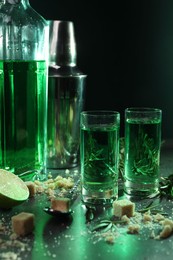 Absinthe in shot glasses, spoon, brown sugar and lime on gray table, closeup. Alcoholic drink