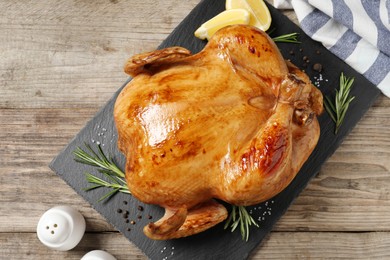 Tasty roasted chicken with spices and lemon on wooden table, top view