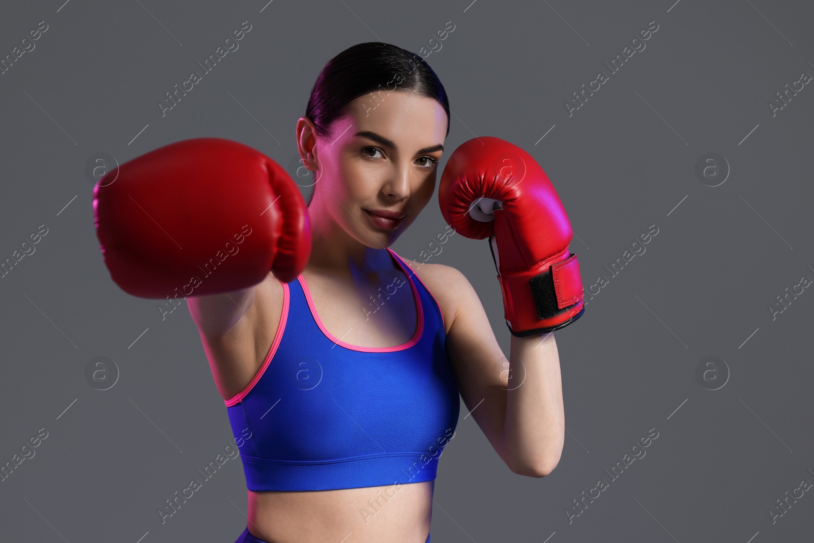 Photo of Portrait of beautiful woman wearing boxing gloves in color lights on grey background