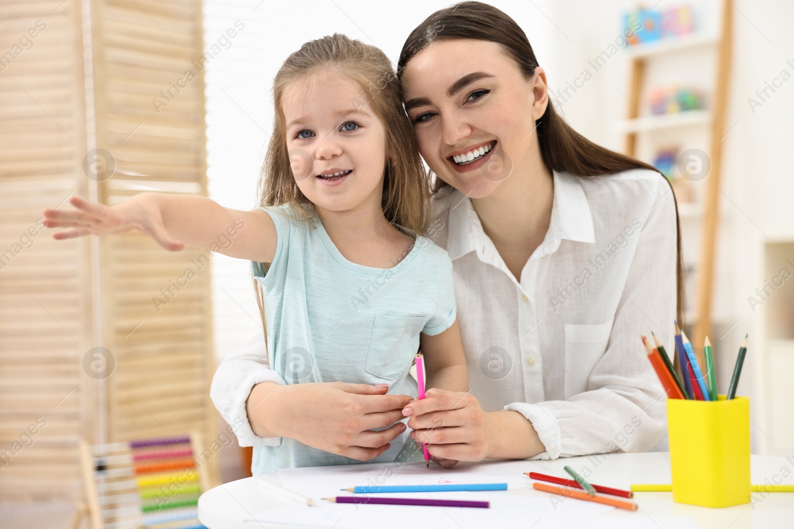 Photo of Mother and her little daughter drawing with colorful pencils at home