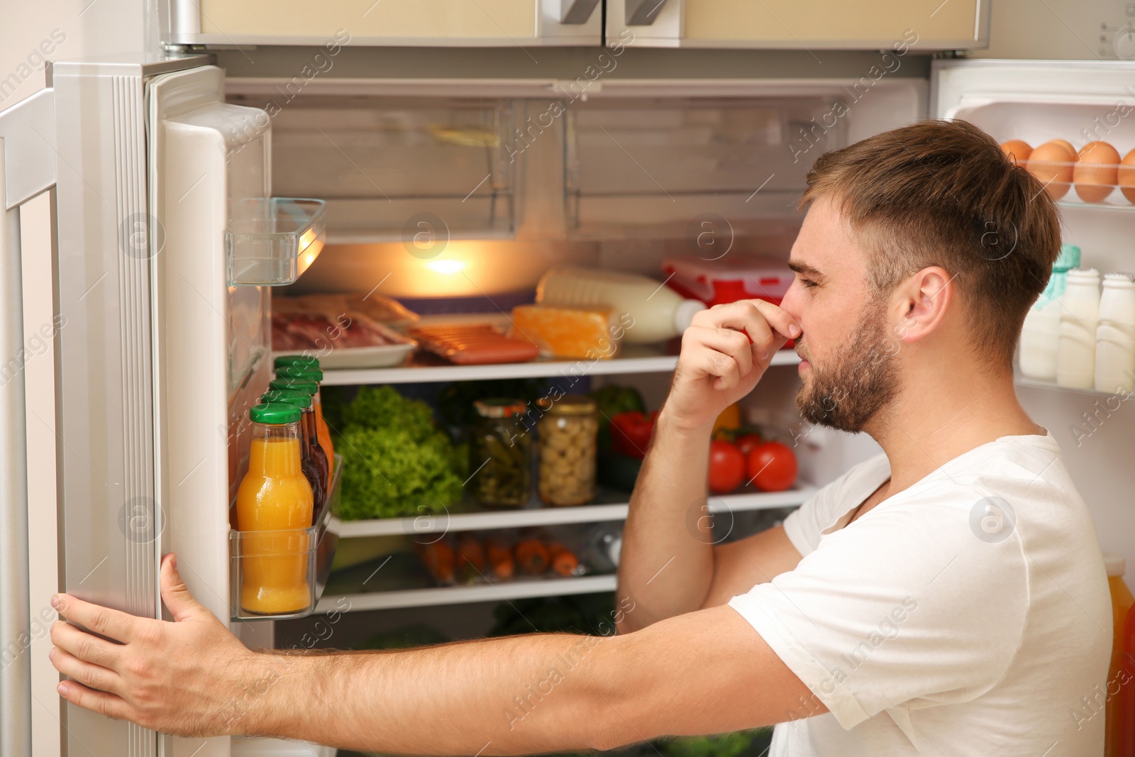 Photo of Young man holding nose cause of bad smell in refrigerator at home